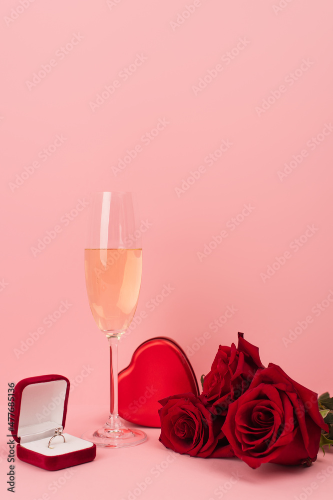glass of champagne near heart-shaped box, roses and engagement ring on pink. glass of champagne near heart-shaped box, roses and engagement ring on pink.