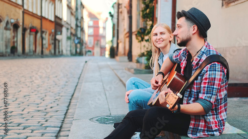 Tourists sitting on sidewalk, playing guitar and having rest. Sightseeing in beautiful european city.