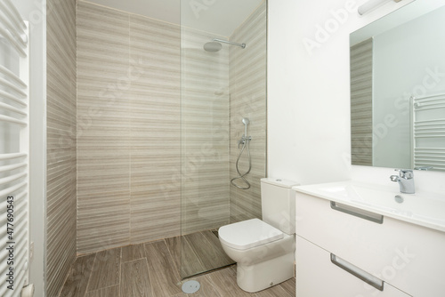 white toilet with wood look tile floors wall mounted radiator mirror and spacious glass top shower