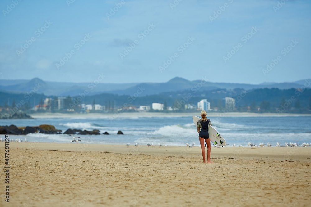 A woman walking on the beach with her surfboard 