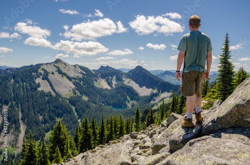 An athletic adventurous man standing on top of a mountain looking at a mountain range.