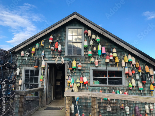 A shingled cottage in Maine with lobster buoys hanging off of it with lobster traps nearby photo