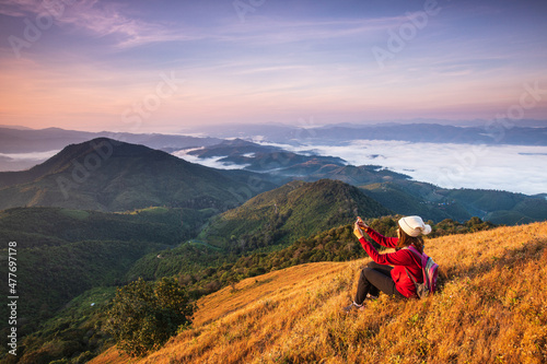 Young woman in red jacket hiking on high mountains and sea of mist . Doi Pui Ko, Mae Hong Son Province, Thailand.