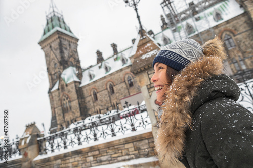 Ottawa winter city Asian woman walking by Canadian Parliament in Ontario, Canada. Travel tourist visiting popular attraction during snowfall wearing cold weather hat and jacket. photo