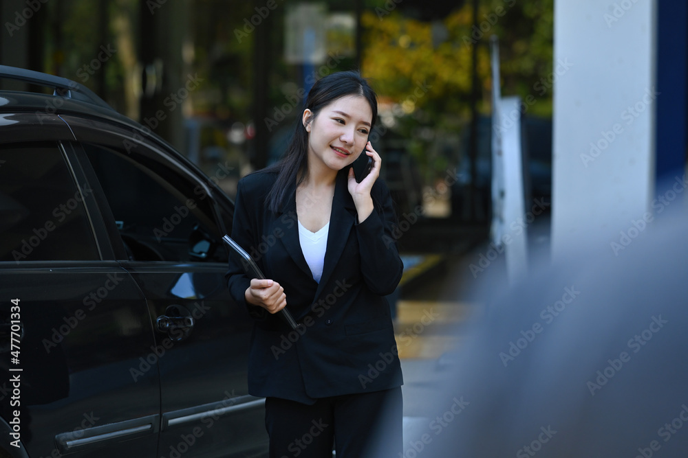Photo of an insurance agent talking on mobile phone while standing with the digital tablet over a black SUV car as a background. Photo of an insurance agent talking on mobile phone while standing with the digital tablet over a black SUV car as a background.