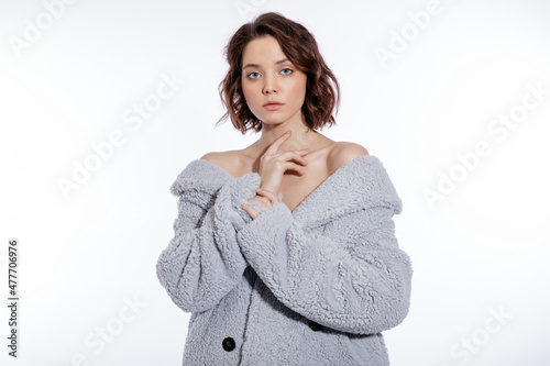 High fashion photo of a beautiful elegant young woman in a pretty pale blue fur coat, suede boots posing over white background. Make up, hairstyle. Slim figure.