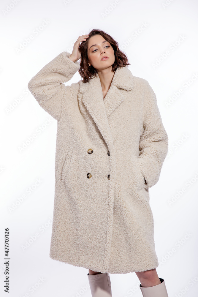 High fashion photo of a beautiful elegant young woman in a pretty cream beige fur coat, boots posing over white background. Make up, hairstyle. Slim figure. High fashion photo of a beautiful elegant young woman in a pretty cream beige fur coat, boots posing over white background. Make up, hairstyle. Slim figure.