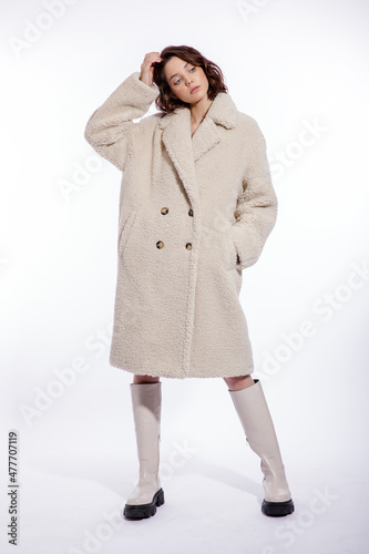 High fashion photo of a beautiful elegant young woman in a pretty cream beige fur coat,  boots posing over white background. Make up, hairstyle. Slim figure.