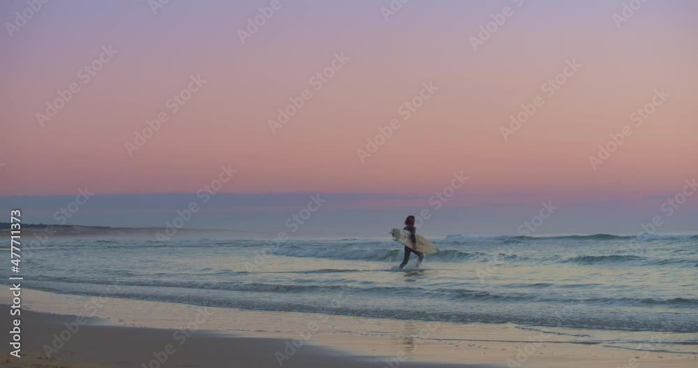 Surfer With Surfboard Running In The Ocean To Surf At Dusk. - wide shot Surfer With Surfboard Running In The Ocean To Surf At Dusk. - wide shot