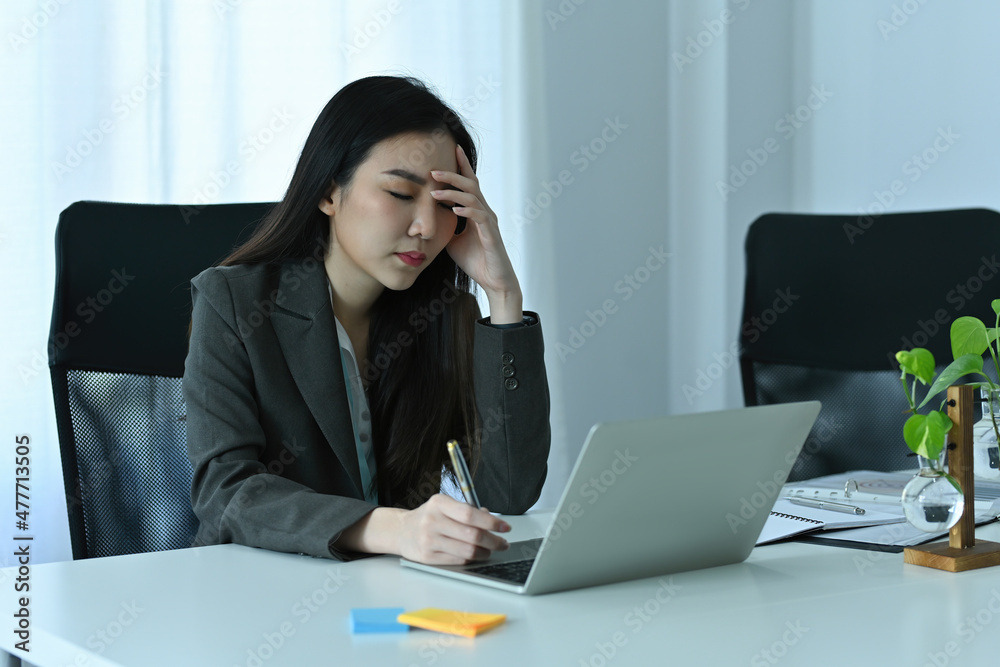 Photo of exhausted office woman sitting in front of a computer laptop at the modern working desk. Photo of exhausted office woman sitting in front of a computer laptop at the modern working desk.