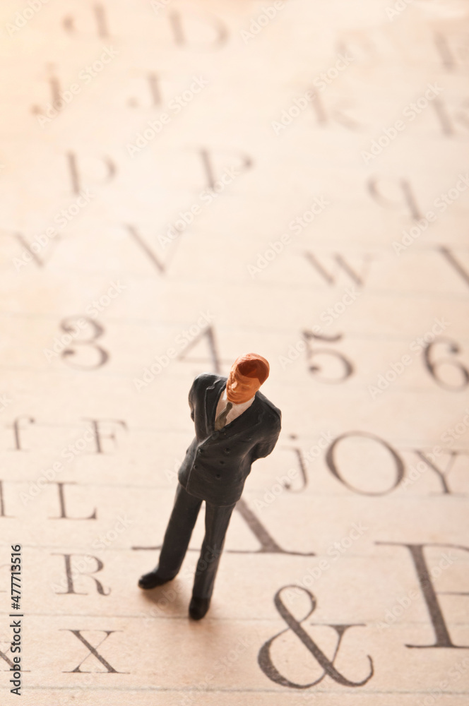 male miniature figurine standing on an alphabet page, literacy and culture concept male miniature figurine standing on an alphabet page, literacy and culture concept