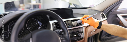 Manual cleaning of car interior with brush for hard-to-reach places in dashboard closeup