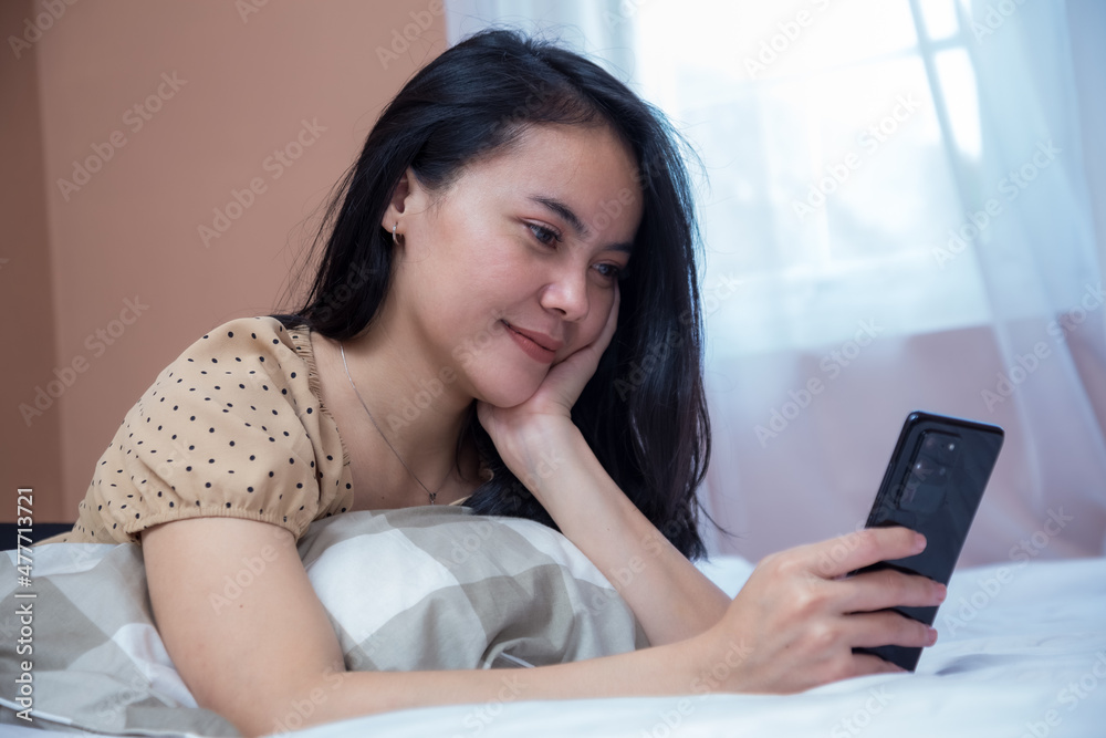 Beautiful woman lying in bed while holding cell phone Beautiful woman lying in bed while holding cell phone