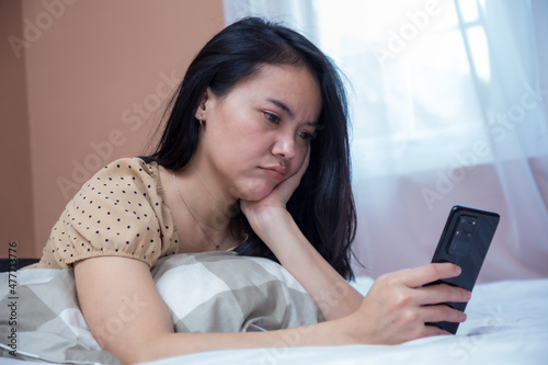 Woman lying on bed with duck lips expression while holding cell phone