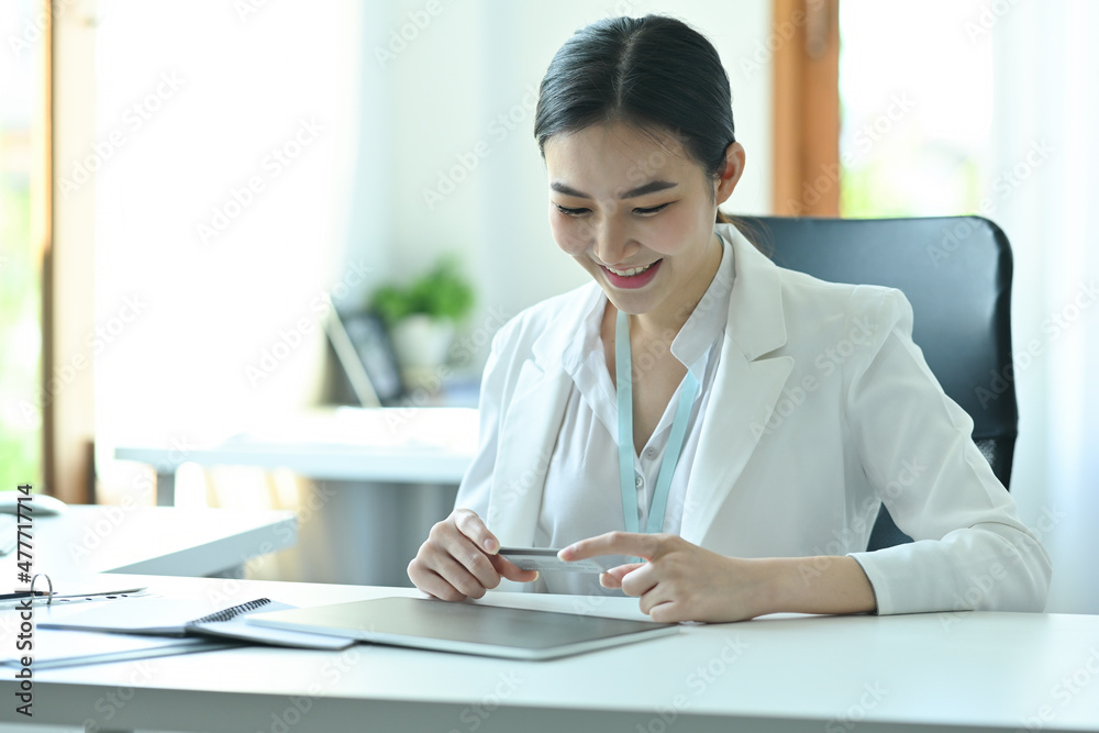 Photo of a confident businesswoman holding a credit card and looking at the digital tablet at the modern working desk. Photo of a confident businesswoman holding a credit card and looking at the digital tablet at the modern working desk.