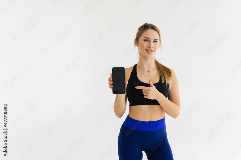 Attractive cheerful young fitness woman showing blank smartphone screen over white background Attractive cheerful young fitness woman showing blank smartphone screen over white background