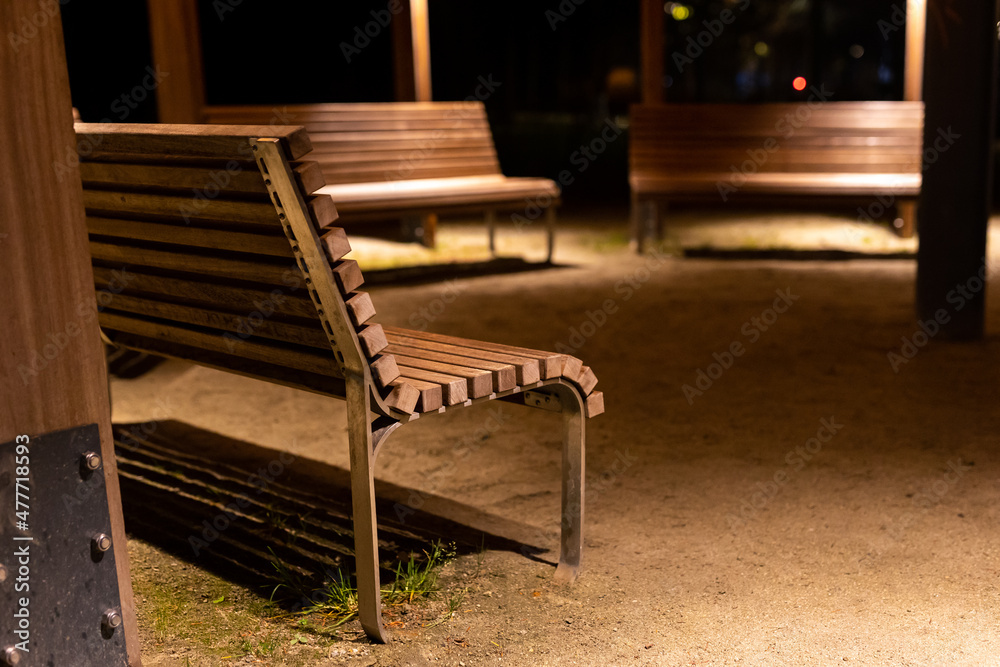 A park shed with empty benches during a pandemic. Meeting places without people. The photo was taken at night with artificial street lighting.