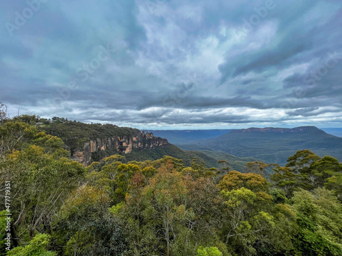 The Three Sisters rocks at Blue Mountains with view of dark clouds covering the rainforest trees, Sydney Australia.