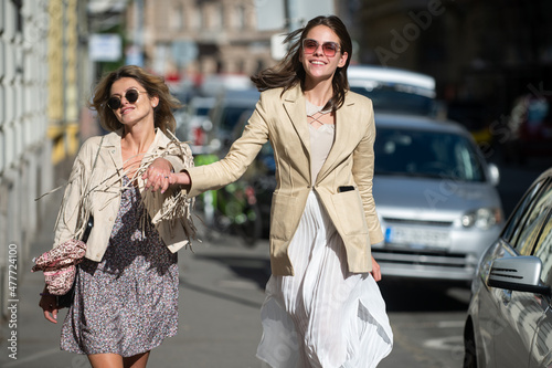 Excited happy women walking together on the street. Happy beautiful women friends in fashion dress walking and running joyful and cheerful smiling in city.