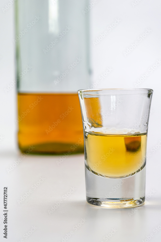 Alcoholic drink in a glass and bottle of brandy in the back on white table. Of strong alcoholic intoxication. The concept of alcohol dependence. Alcohol intoxication. Alcoholic drink in a glass and bottle of brandy in the back on white table. Of strong alcoholic intoxication. The concept of alcohol dependence. Alcohol intoxication.