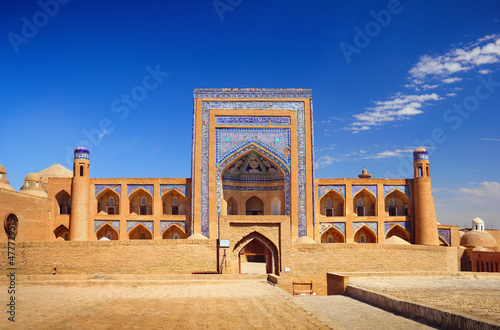 Beautiful old city, ancient Allakuli Khan Madrassah (Allah Quli Madrasa), at the background of bright blue sky in Historic Center of Khiva (UNESCO World Heritage Site), Uzbekistan, Central Asia
