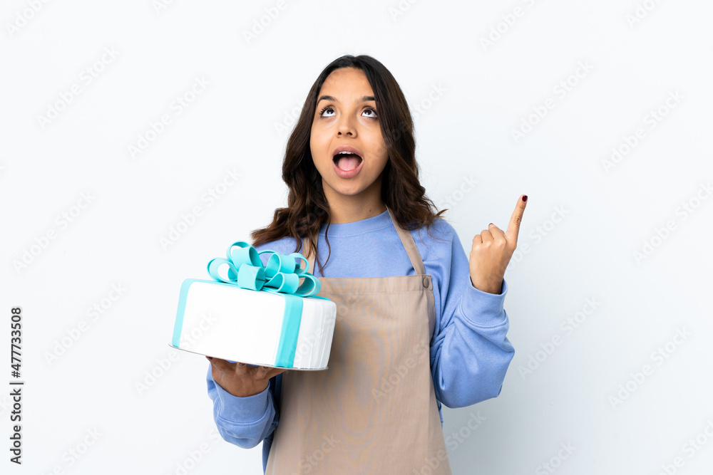 Pastry chef holding a big cake over isolated white background pointing up and surprised Pastry chef holding a big cake over isolated white background pointing up and surprised
