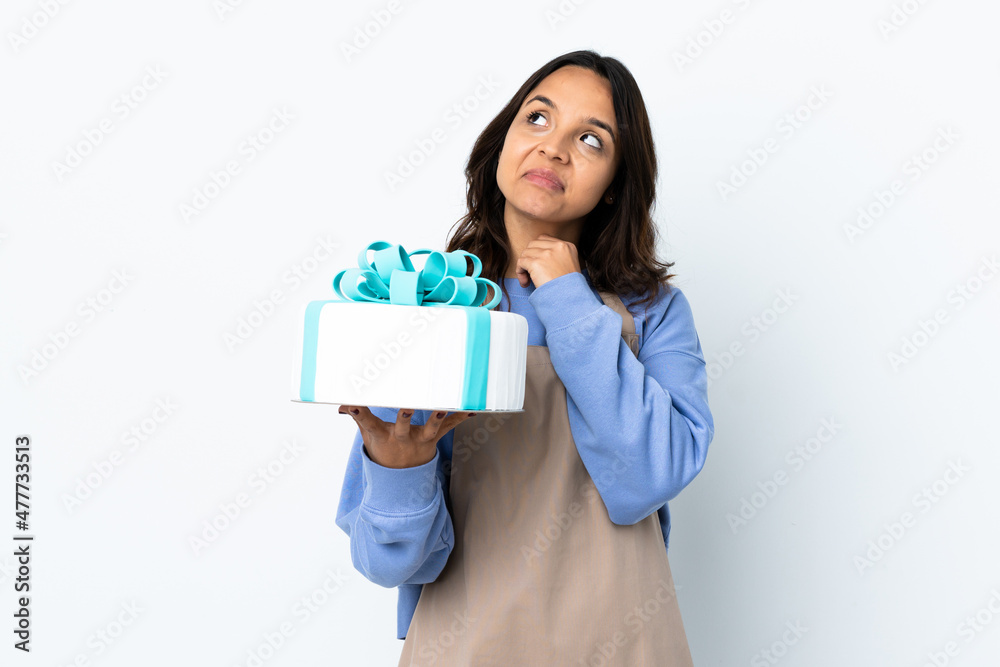 Pastry chef holding a big cake over isolated white background looking up while smiling Pastry chef holding a big cake over isolated white background looking up while smiling