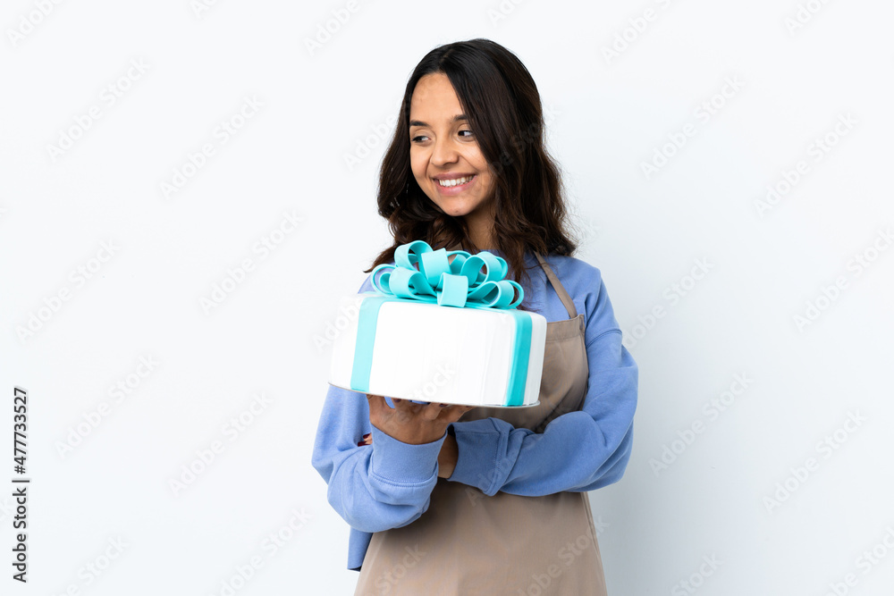 Pastry chef holding a big cake over isolated white background looking to the side and smiling Pastry chef holding a big cake over isolated white background looking to the side and smiling