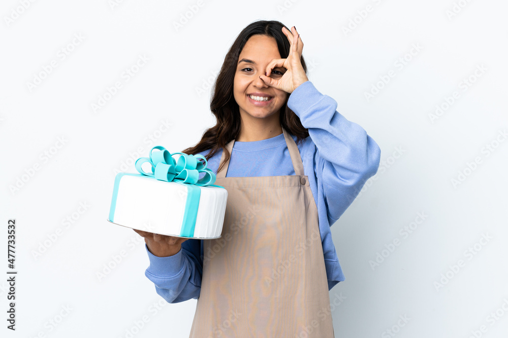 Pastry chef holding a big cake over isolated white background showing ok sign with fingers Pastry chef holding a big cake over isolated white background showing ok sign with fingers