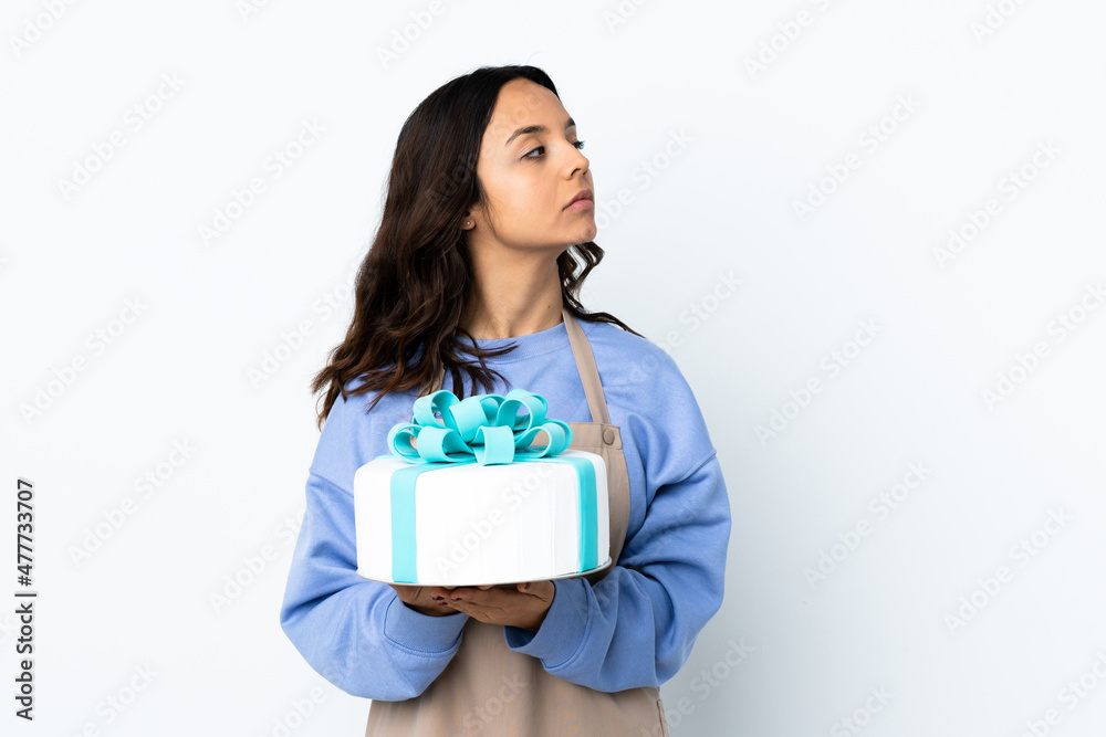 Pastry chef holding a big cake over isolated white background keeping the arms crossed Pastry chef holding a big cake over isolated white background keeping the arms crossed