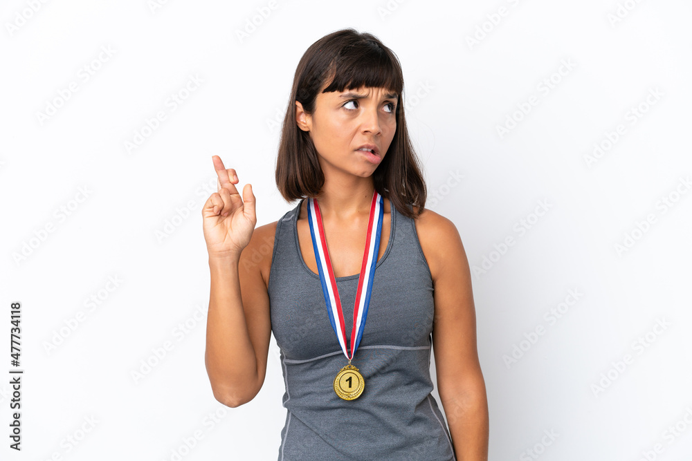 Young mixed race woman with medals isolated on white background with fingers crossing and wishing the best Young mixed race woman with medals isolated on white background with fingers crossing and wishing the best