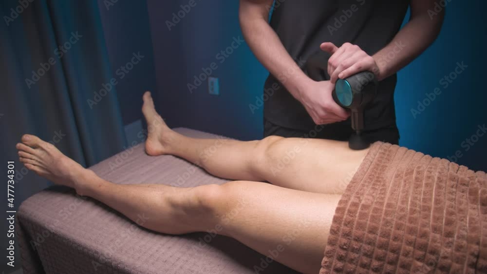 Man male masseur massages the leg of a male athlete client with a massage percussion apparatus. Shock wave therapy Man male masseur massages the leg of a male athlete client with a massage percussion apparatus. Shock wave therapy