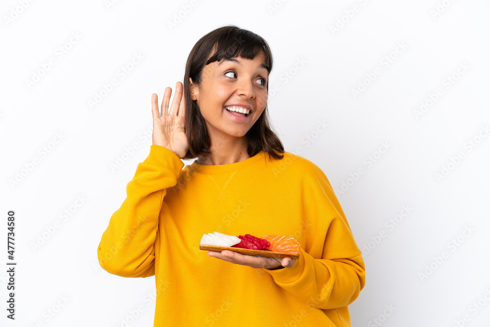 Young mixed race woman holding sashimi isolated on white background listening to something by putting hand on the ear Young mixed race woman holding sashimi isolated on white background listening to something by putting hand on the ear