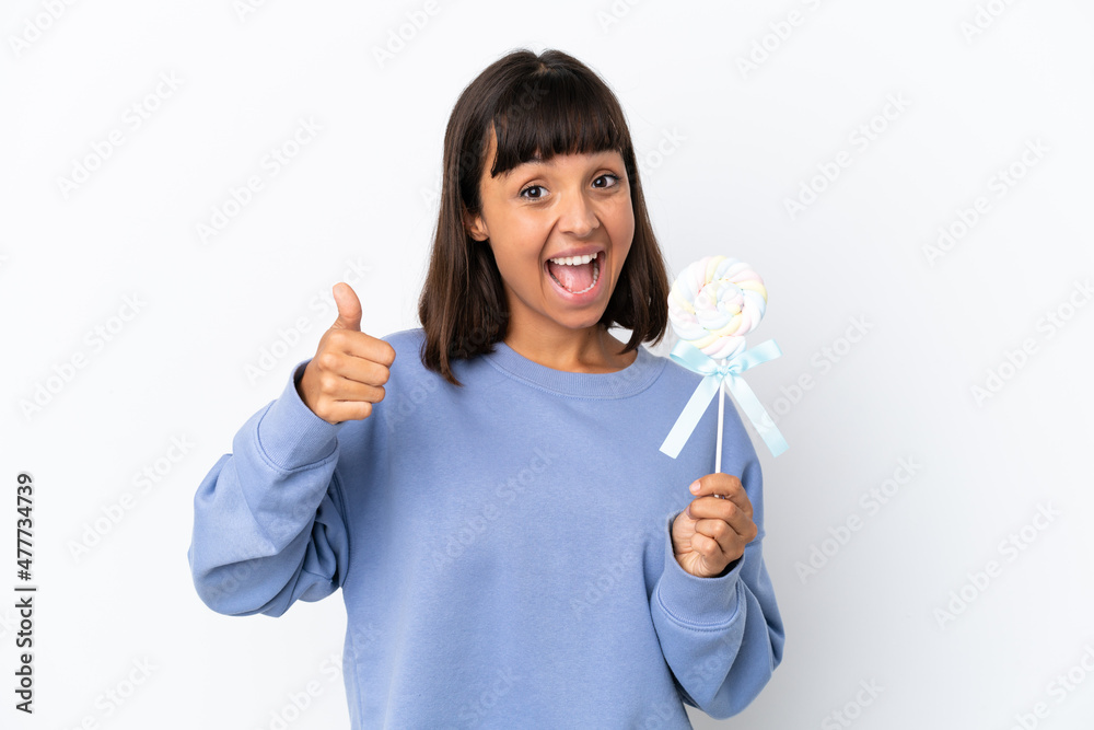 Young mixed race woman holding a lollipop isolated on white background with thumbs up because something good has happened Young mixed race woman holding a lollipop isolated on white background with thumbs up because something good has happened