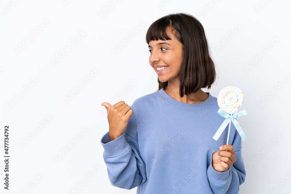 Young mixed race woman holding a lollipop isolated on white background pointing to the side to present a product Young mixed race woman holding a lollipop isolated on white background pointing to the side to present a product