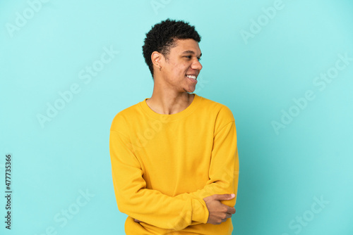 Young African American man isolated on blue background looking to the side and smiling