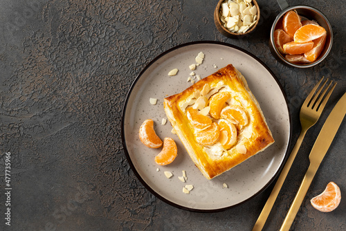 Mini puff pie with cheese cream, almonds, and tangerines in a plate on the kitchen table. Delicious layered square with citrus fruits, dorblue or ricotta, nuts on a culinary background top view photo