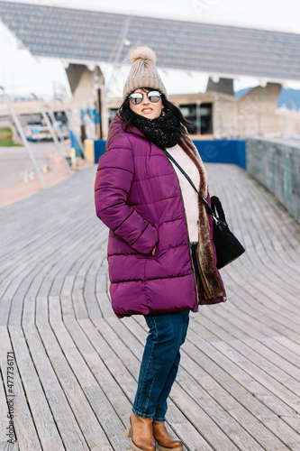 portrait of a smiling woman with sunglasses and wool cap on a sunny autumn day walking in the city