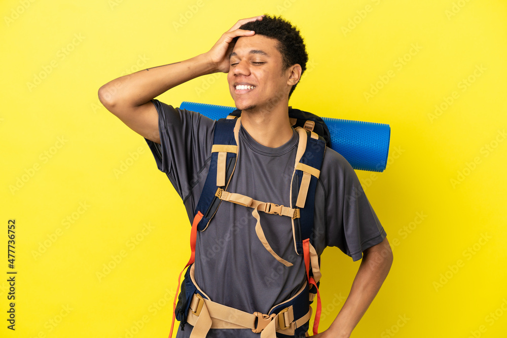 Young mountaineer African American man with a big backpack isolated on yellow background smiling a lot Young mountaineer African American man with a big backpack isolated on yellow background smiling a lot