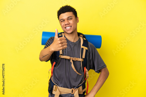 Young mountaineer African American man with a big backpack isolated on yellow background with thumbs up because something good has happened