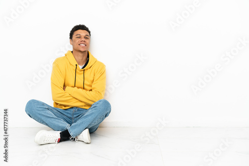 Young African American man sitting on the floor isolated on white background with arms crossed and looking forward