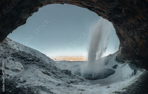 Seljalandsfoss waterfall in Iceland during winter with blue sky and snow and frozen landscape.