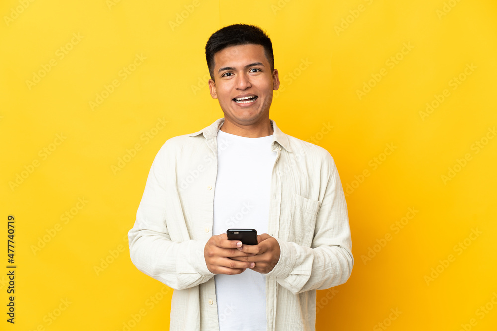 Young Ecuadorian man isolated on yellow background surprised and sending a message Young Ecuadorian man isolated on yellow background surprised and sending a message