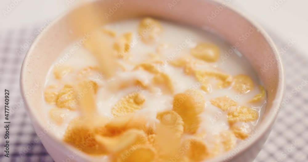 Close-up of dry breakfast corn flakes falling into milk in a bowl served on a table