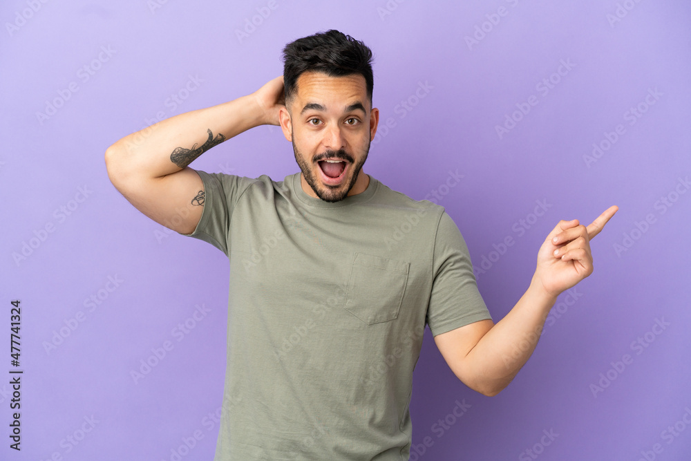 Young caucasian man isolated on purple background surprised and pointing finger to the side Young caucasian man isolated on purple background surprised and pointing finger to the side