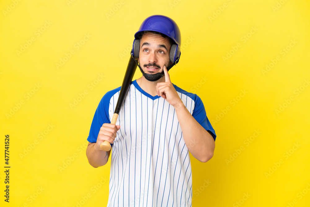 Young caucasian man playing baseball isolated on yellow background thinking an idea while looking up