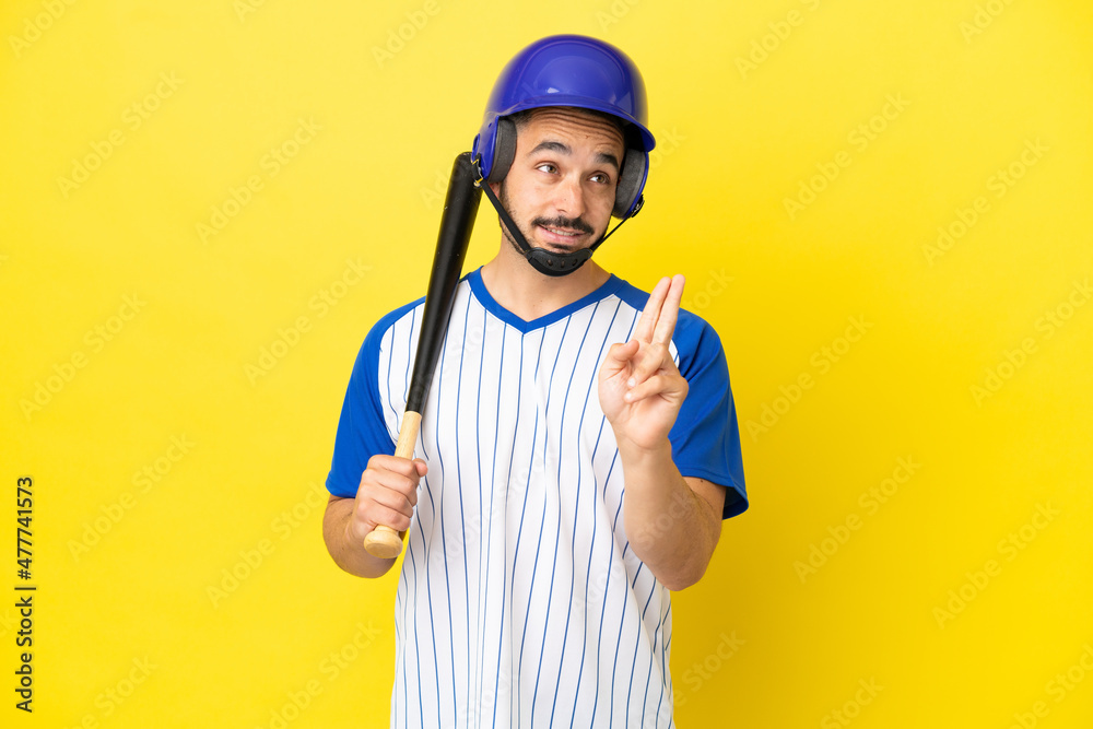 Young caucasian man playing baseball isolated on yellow background with fingers crossing and wishing the best