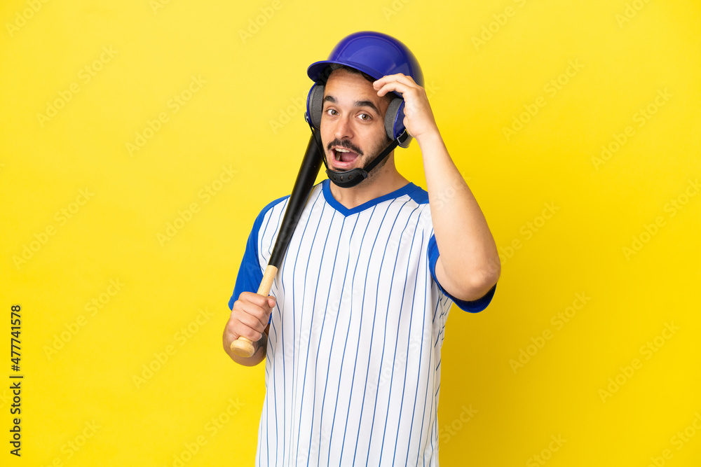 Young caucasian man playing baseball isolated on yellow background doing surprise gesture while looking to the side