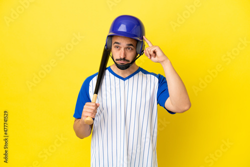 Young caucasian man playing baseball isolated on yellow background having doubts and thinking