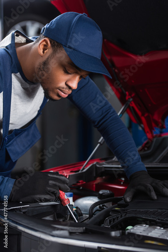 african american foreman with screwdriver making diagnostics of car engine.